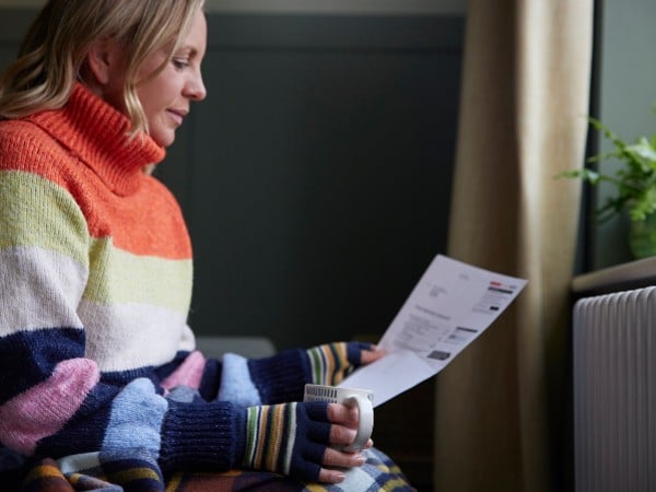 A woman in gloves and a jumper reading a bill