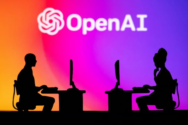 People sat working against backdrop of OpenAI logo