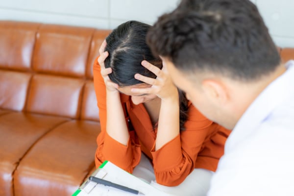 A person with their head in their hands as their manager talks to them