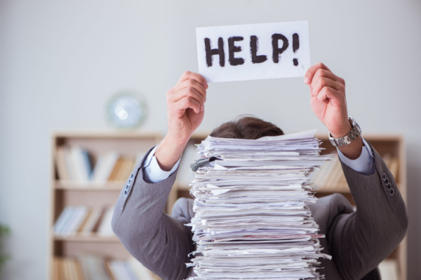 Image of a man holding up a "HELP" sign at his desk