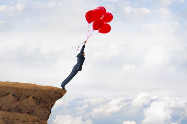 A man holding onto some balloons as he stands over a cliff