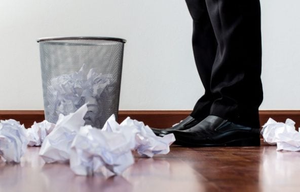 A person stood next to a rubbish bin, which is filled with crumpled up paper