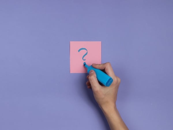 Person writing question mark on a post it note