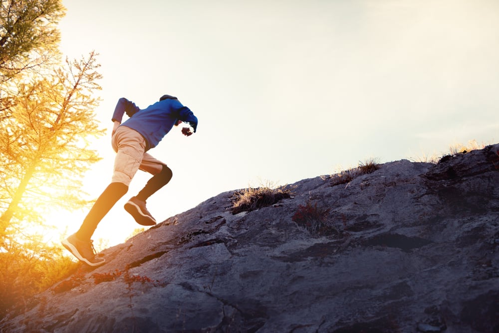 Man runs uphill by big rock against sunset sky