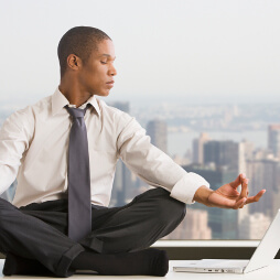 Man in a shirt and tie, in a meditating pose, looking at laptop to his side