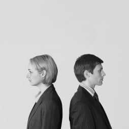 Man and woman, wearing suits, standing back to back, only top half visible