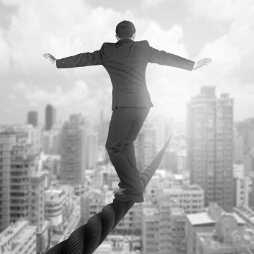 Man in a suit, balancing on a rope, high above buildings