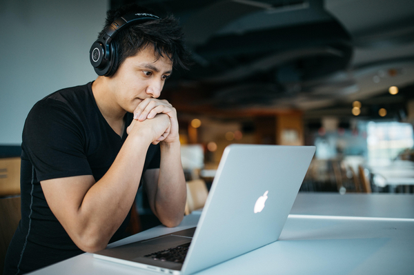 A young man sat at a table with headphones on in front of a laptop