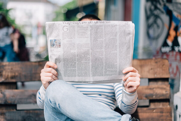 Photo of person sitting on a bench reading a newspaper